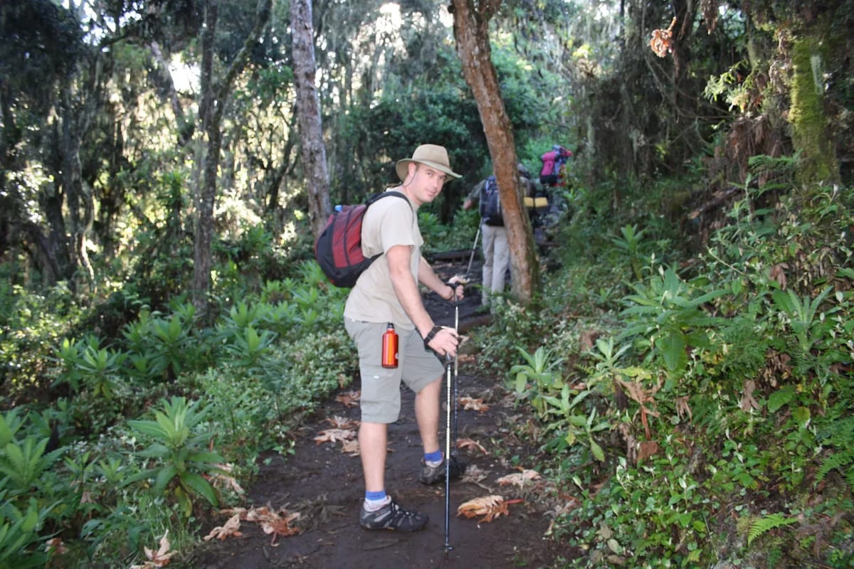 A man with a backpack and hiking poles walks along a trail on Mount Kilimanjaro, surrounded by scenic landscapes.