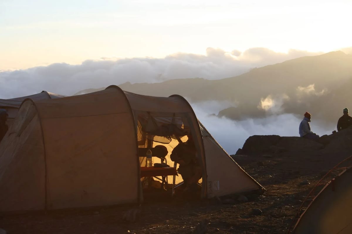 People sitting in tents on Mount Kilimanjaro, surrounded by rocky terrain and a clear blue sky.