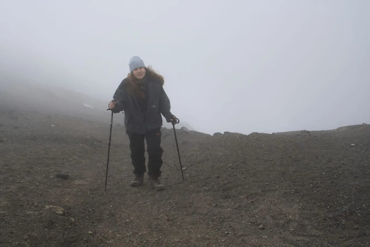 A person using ski poles walks on the slopes of Mount Kilimanjaro, surrounded by rocky terrain and clear skies.