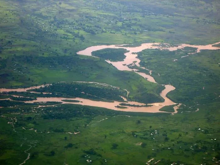 Aerial view of a river flowing through a lush green field, surrounded by natural landscape and grass, showcasing the intricate patterns of the water's path.